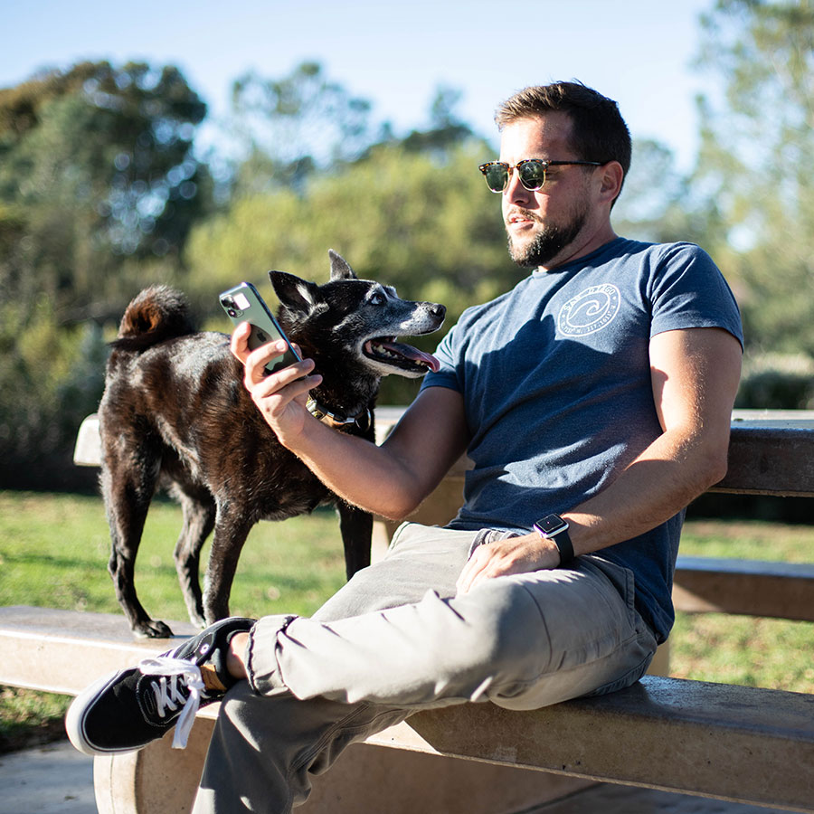 pet parent sitting on park bench with dog, while using phone