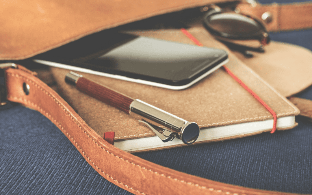 A purse with a pen, planner, sunglasses, and cell phone