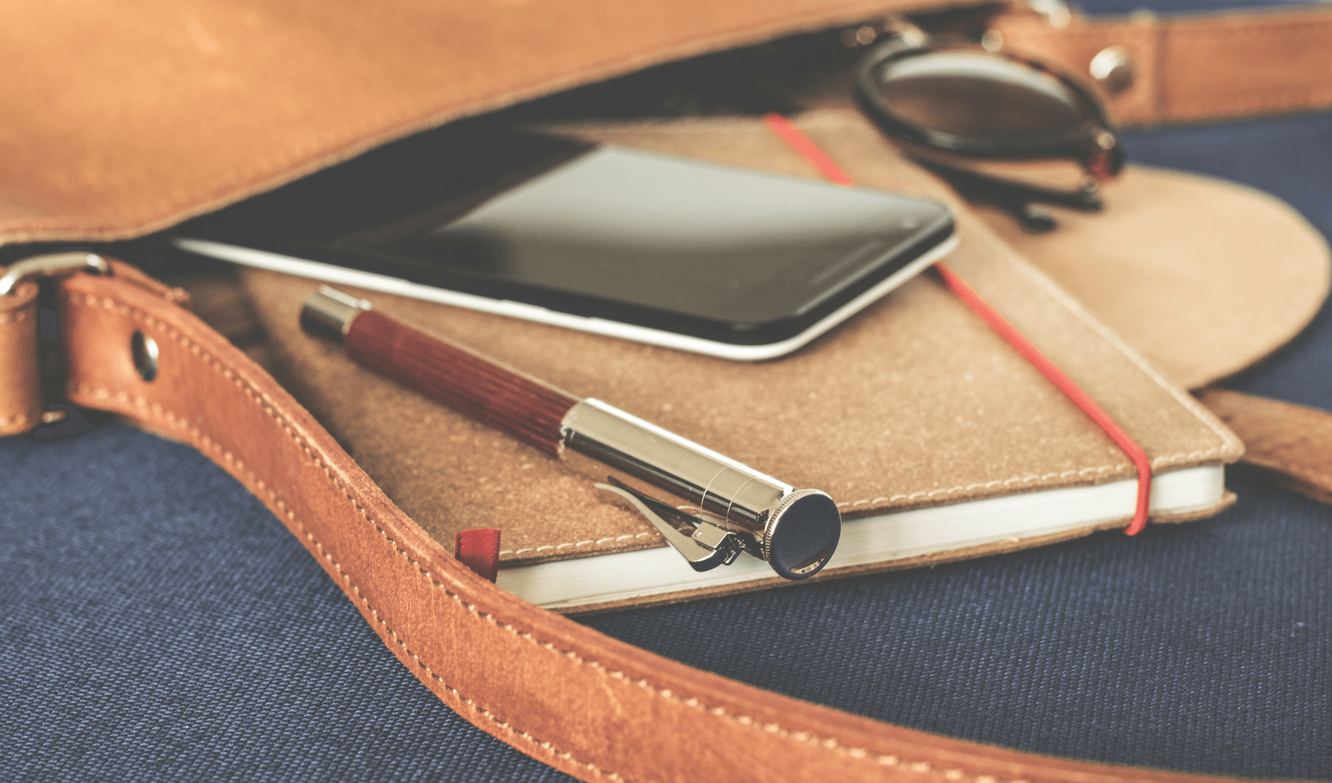 A purse with a pen, planner, sunglasses, and cell phone