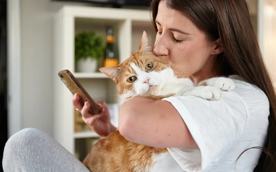 Woman kissing her cat while using her smartphone