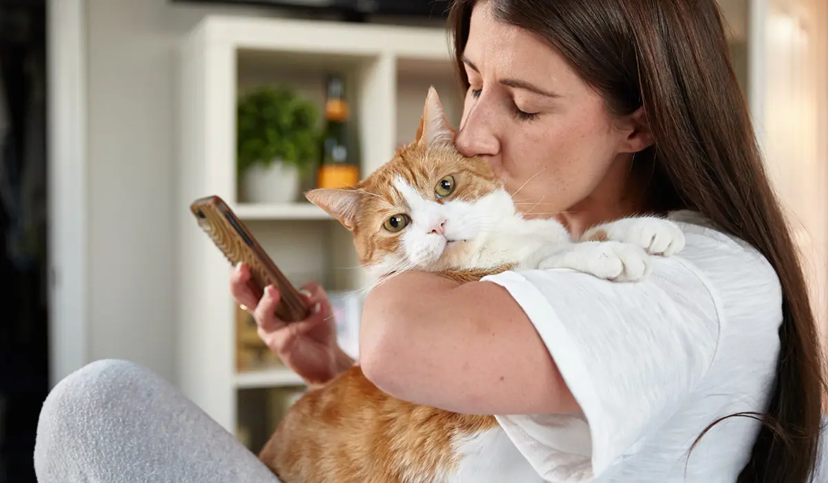 Woman kissing her cat while using her smartphone