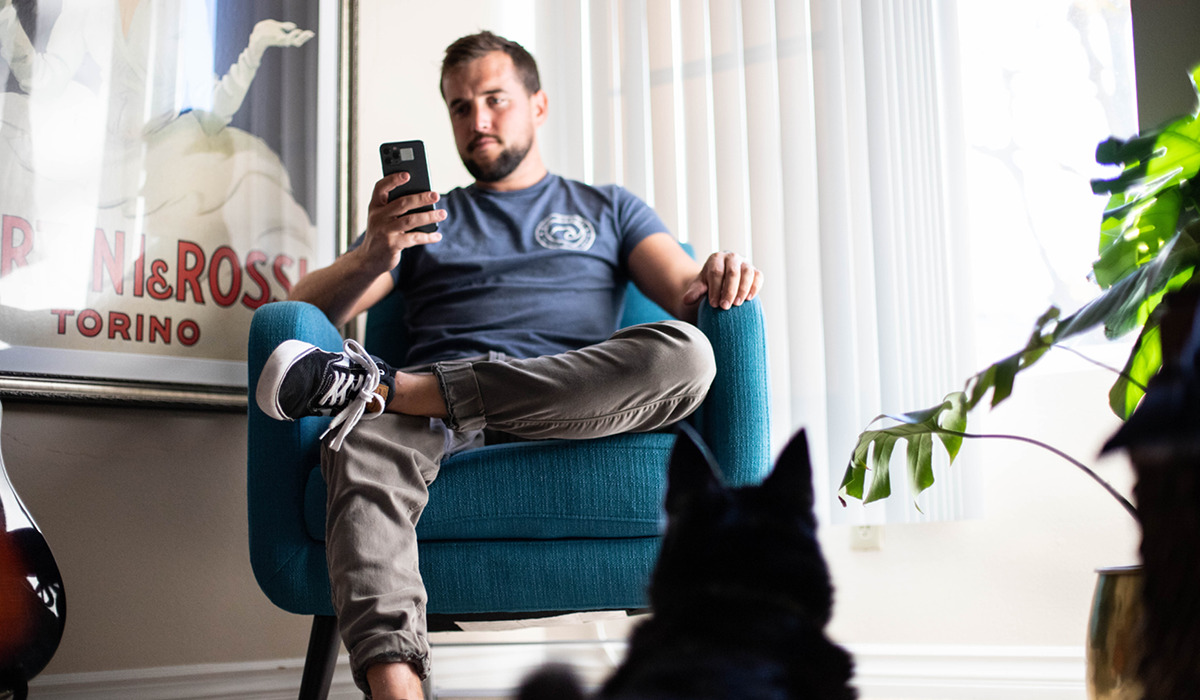 Man using his smartphone while sitting in a chair with his dog watching