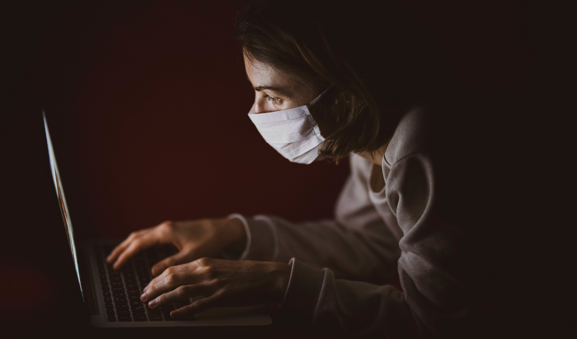 A woman typing on her computer while wearing a face mask