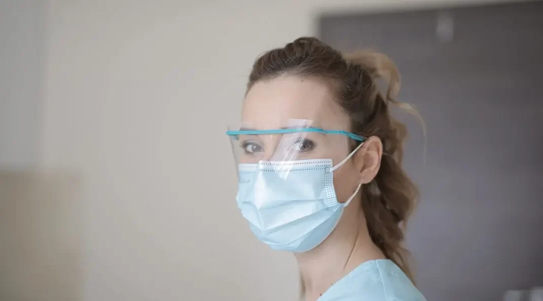 Photo of a veterinary technician looking at the camera while wearing a face mask and protective glasses