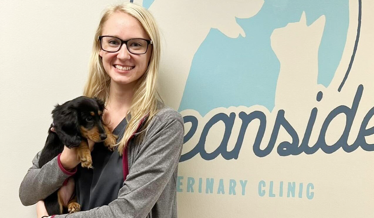 Veterinary Technician holding a puppy<br />
 by the Oceanside Veterinary Clinic logo