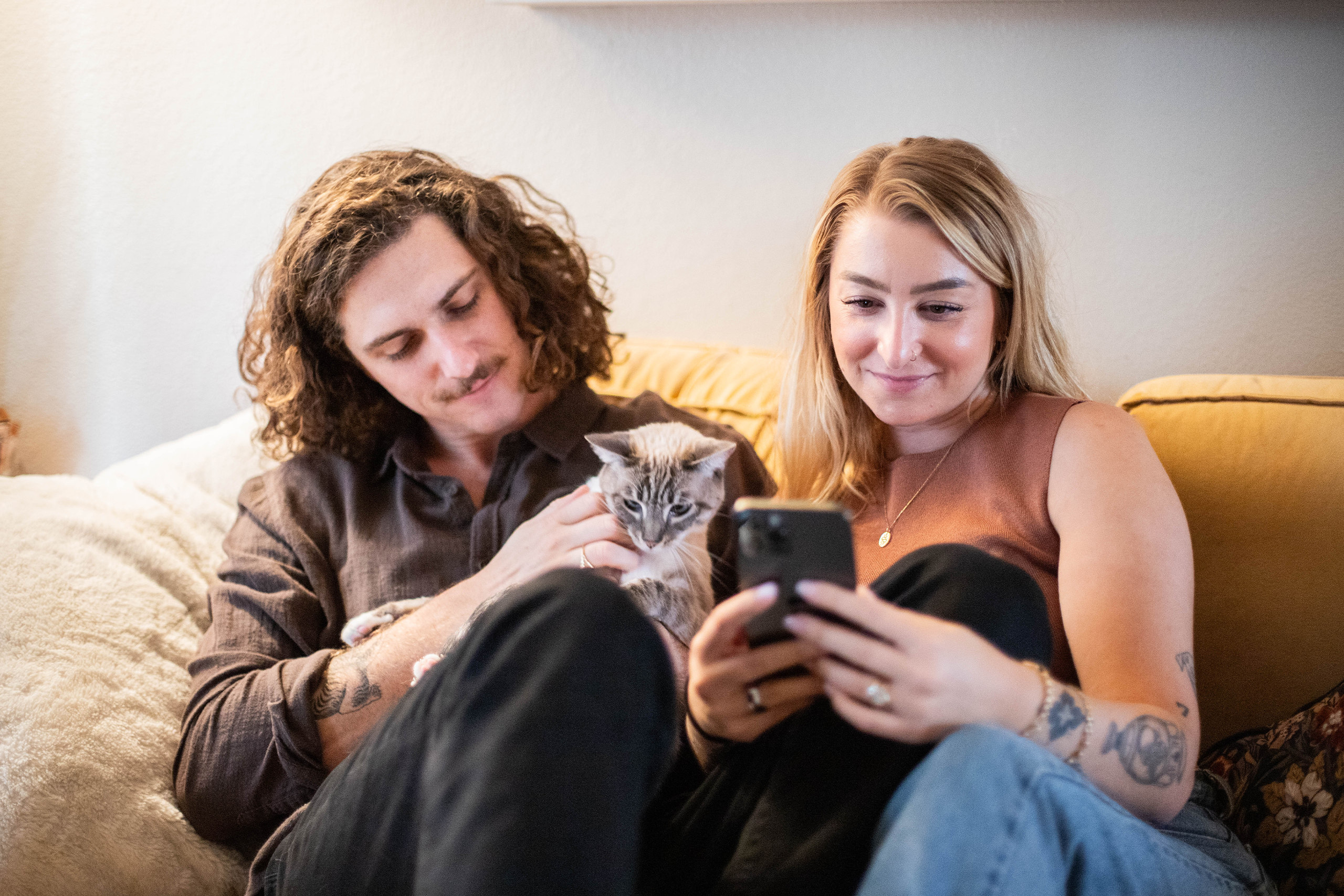 Pet parents sitting together with cat while looking at their phone